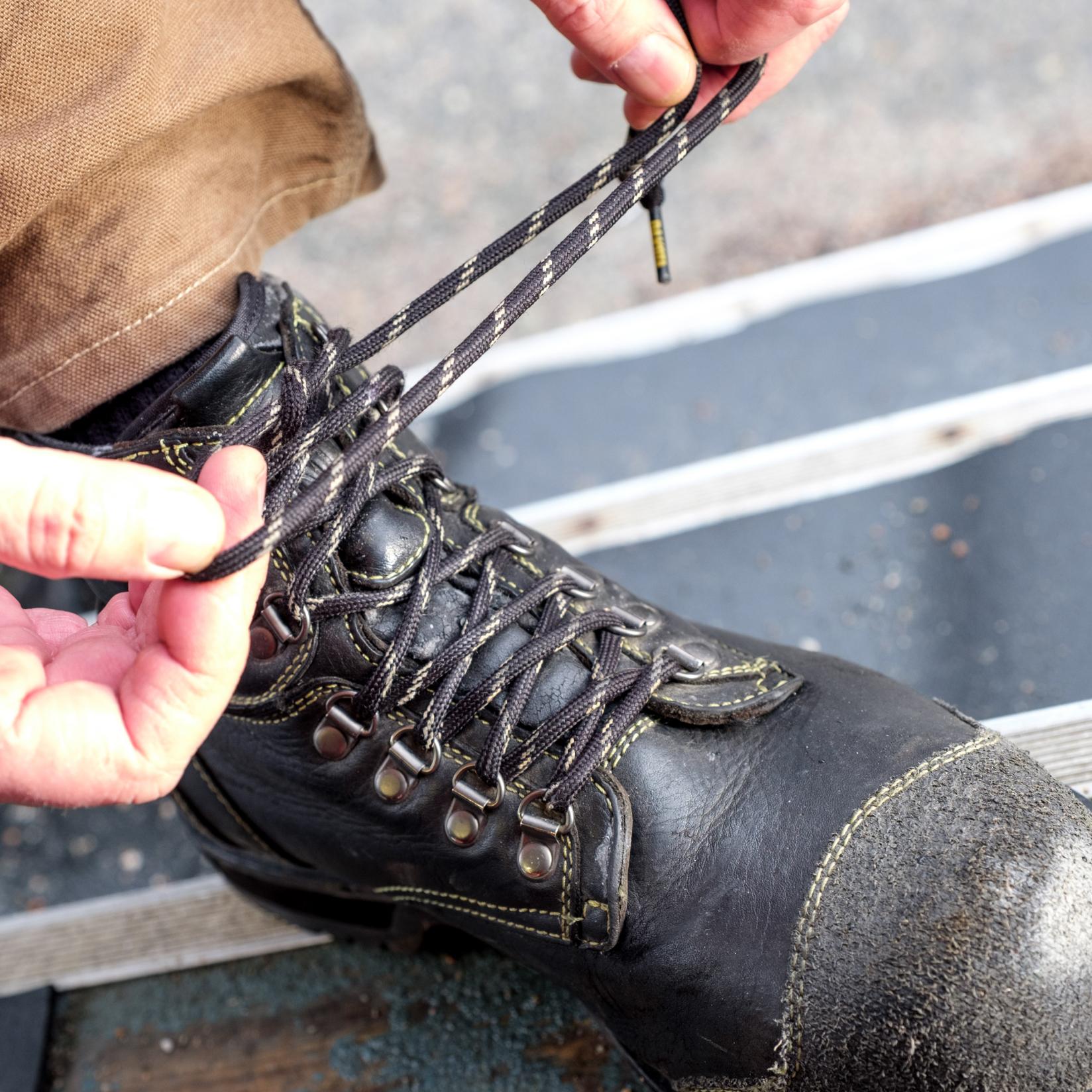Up close shot of a person with their work boot on a bench, tying the laces of their boot.
