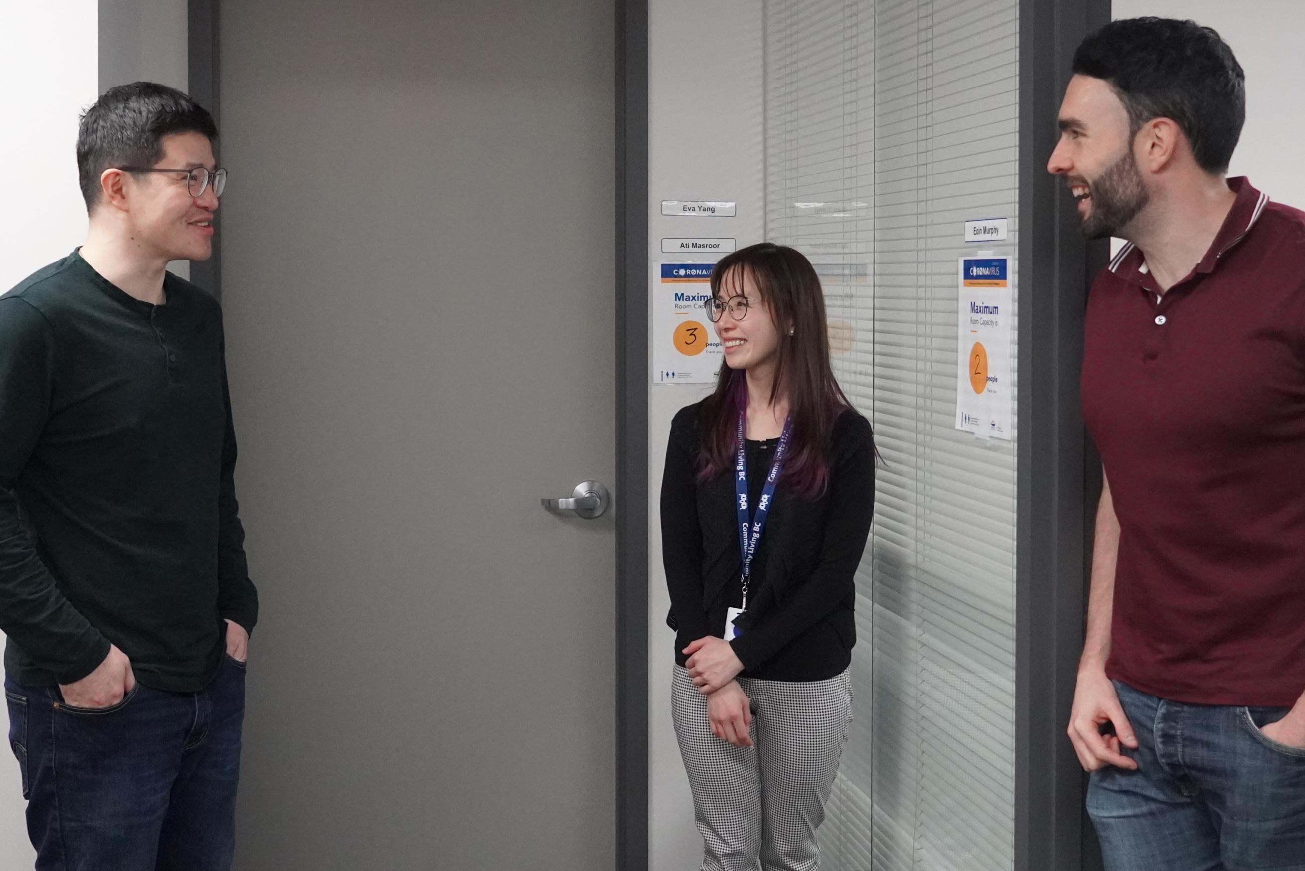 Two men and a woman standing outside offices, engaged in conversation.