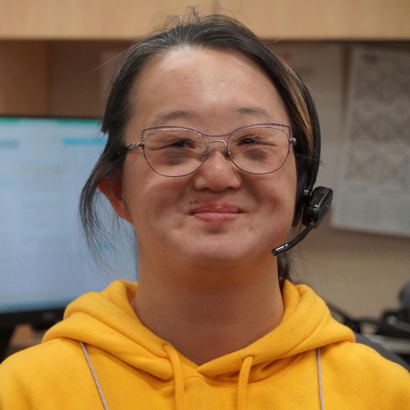 Woman wearing a headset in an office, smiling at the camera.