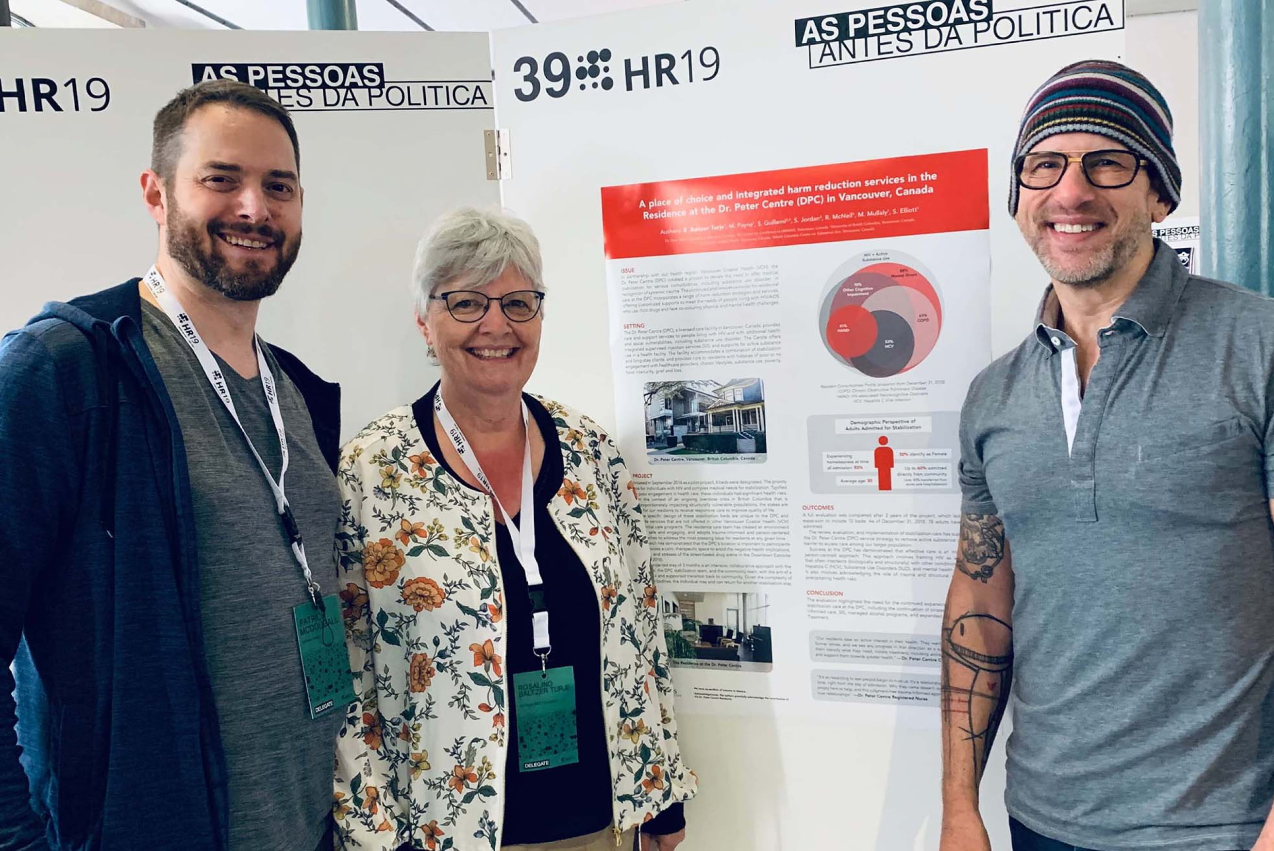 A woman and two men posting for the camera in front of a informational poster for Dr. Peter.