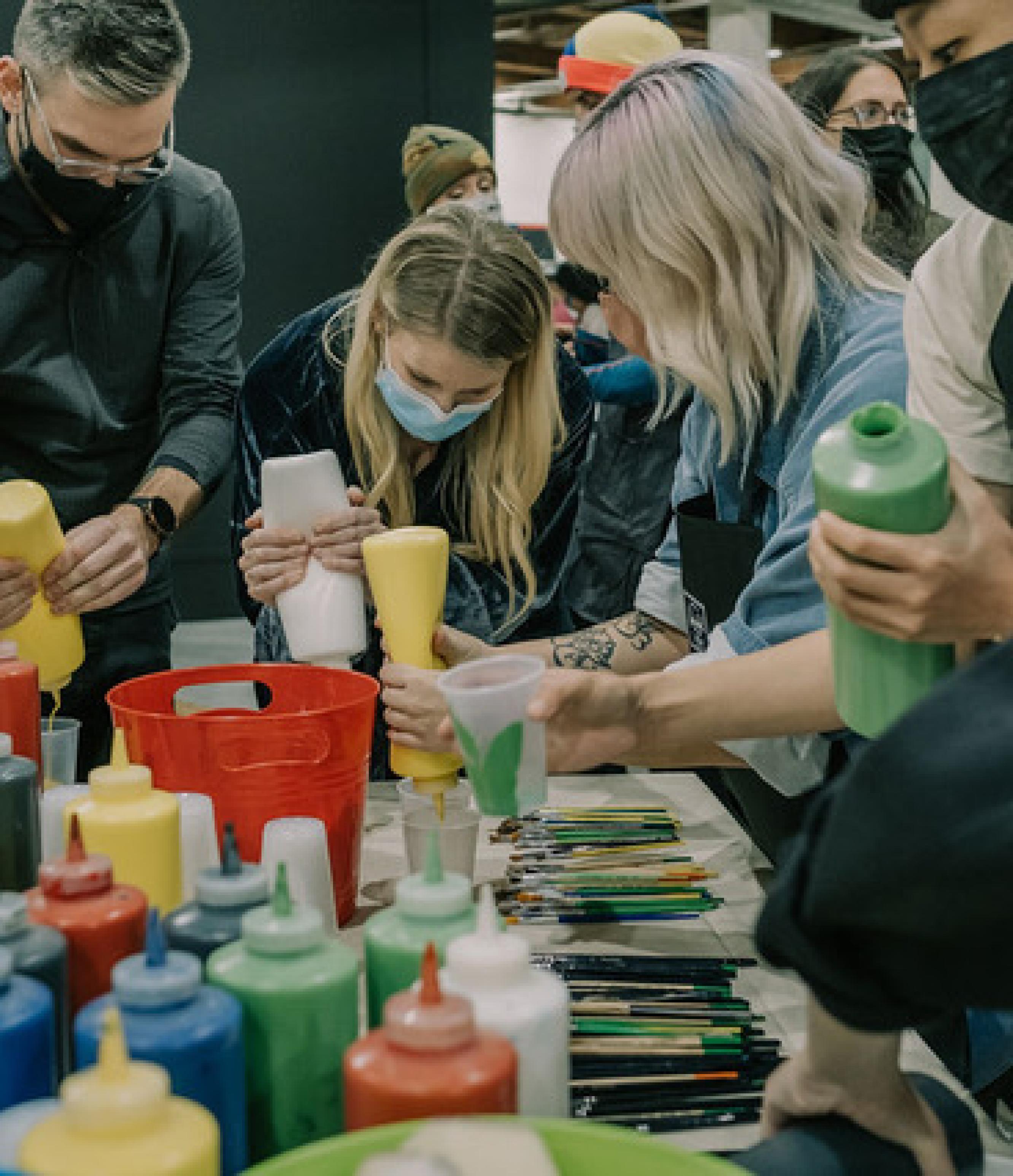 A group of people with masks putting different colours of paint in cups to use.