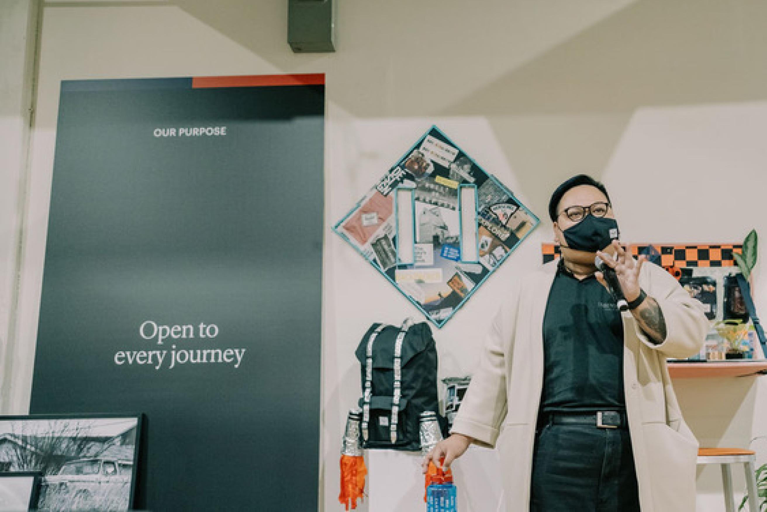 A person in a mask standing and talking to a group of people.
